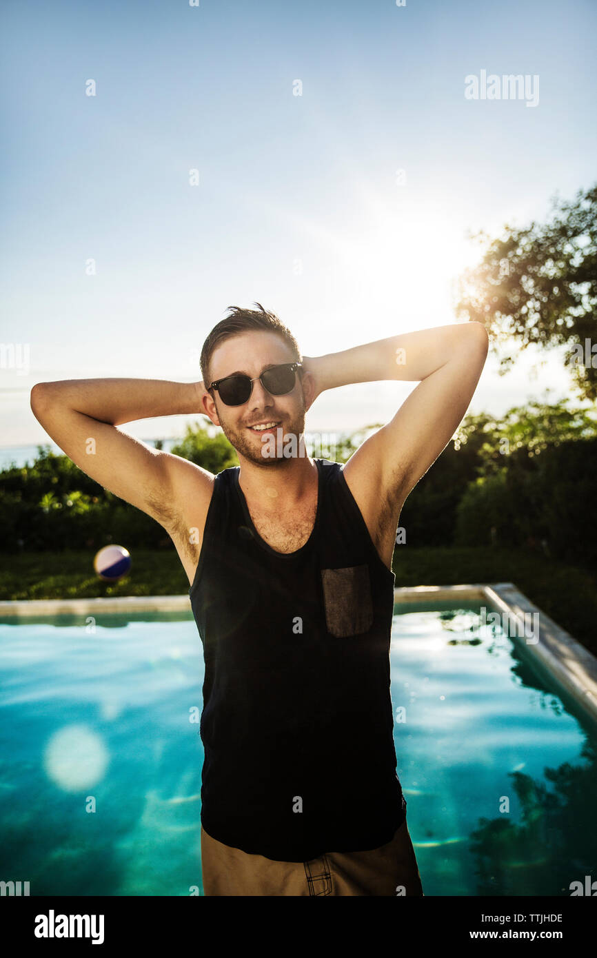 Man with hands behind head standing against pool in backyard Stock Photo