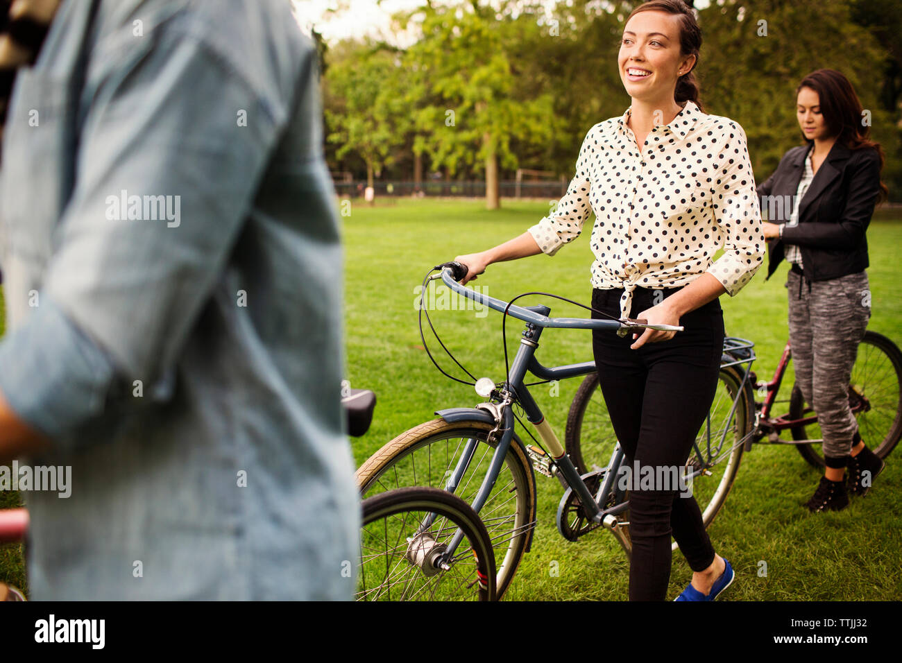 Women with bicycles walking on field in central park Stock Photo