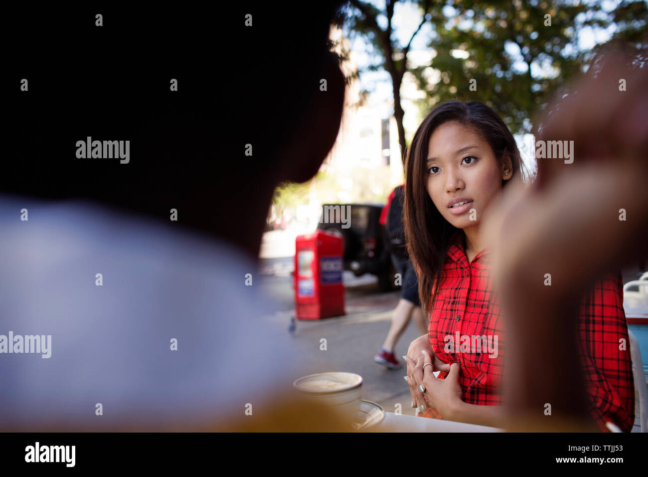 Woman looking at friend while sitting in sidewalk cafe Stock Photo