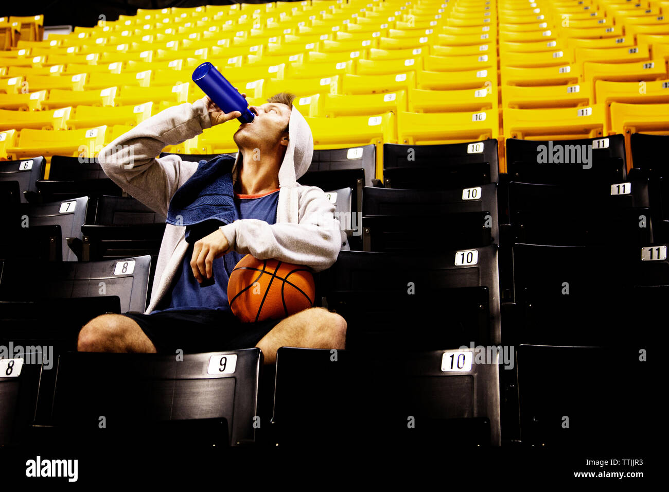 Man with basketball drinking water while sitting on seat in stadium Stock Photo