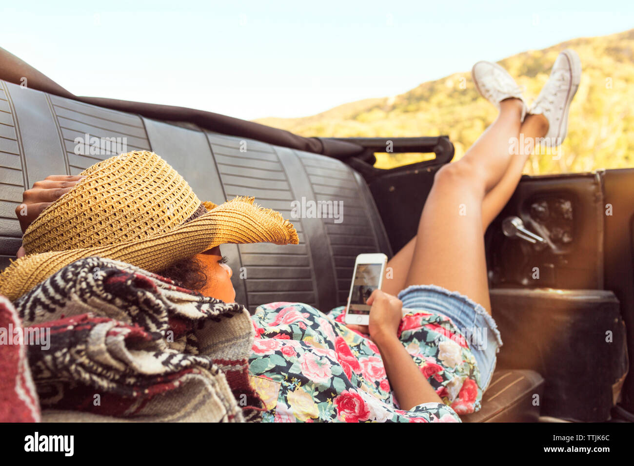 Woman using smart phone while lying in convertible car Stock Photo