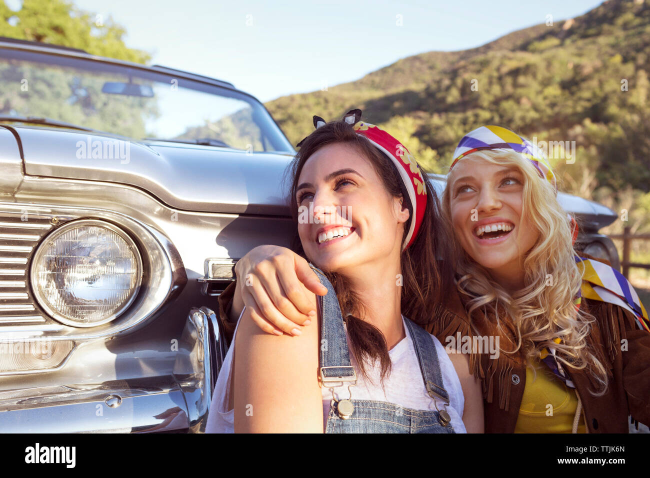 Happy women looking away while sitting against convertible car Stock Photo