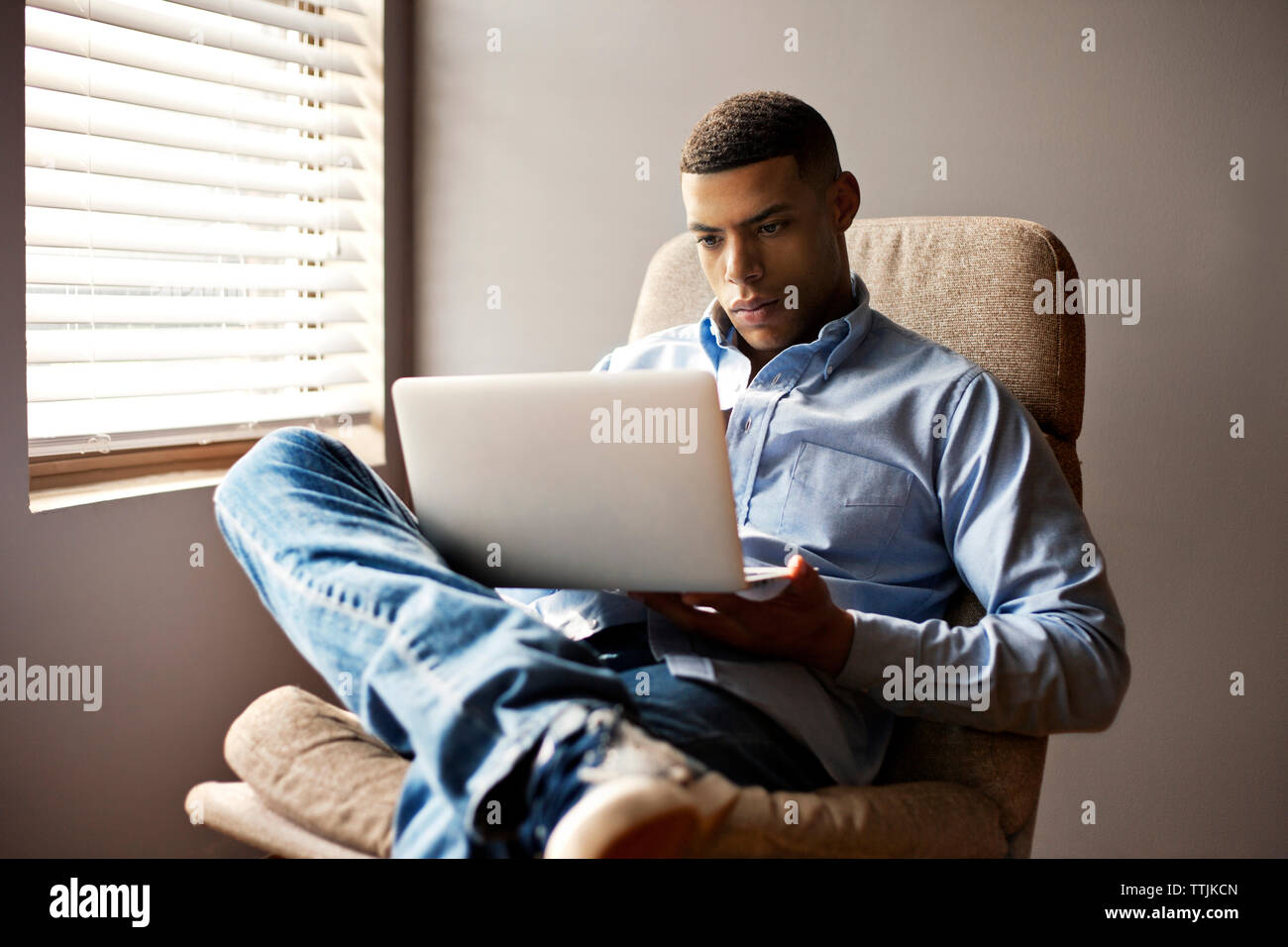 Man using laptop computer while sitting on chair at home Stock Photo
