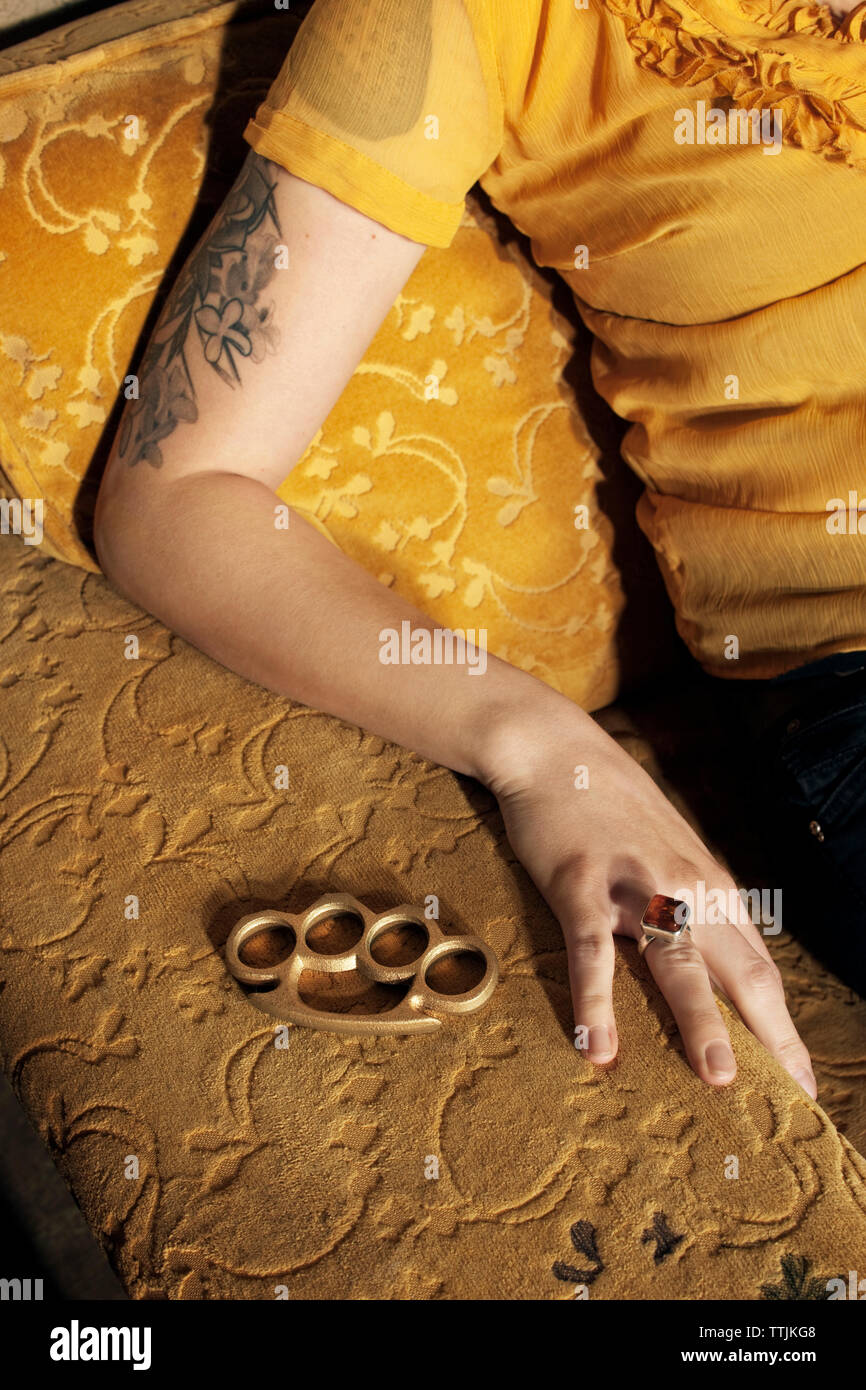 Cropped image of woman with brass knuckle sitting on sofa Stock Photo