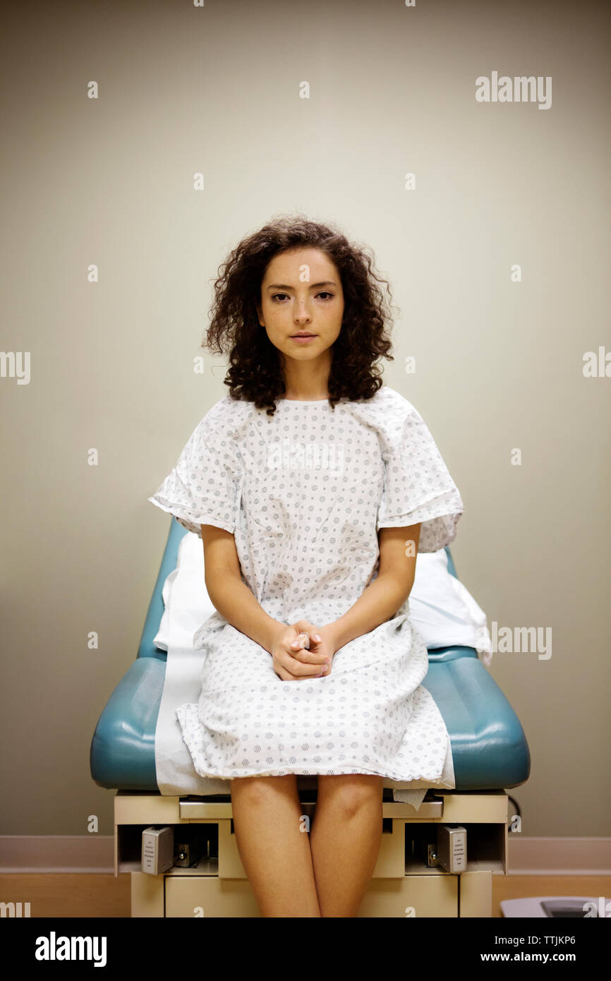 Portrait of woman with hands clasped sitting on bed in hospital Stock Photo
