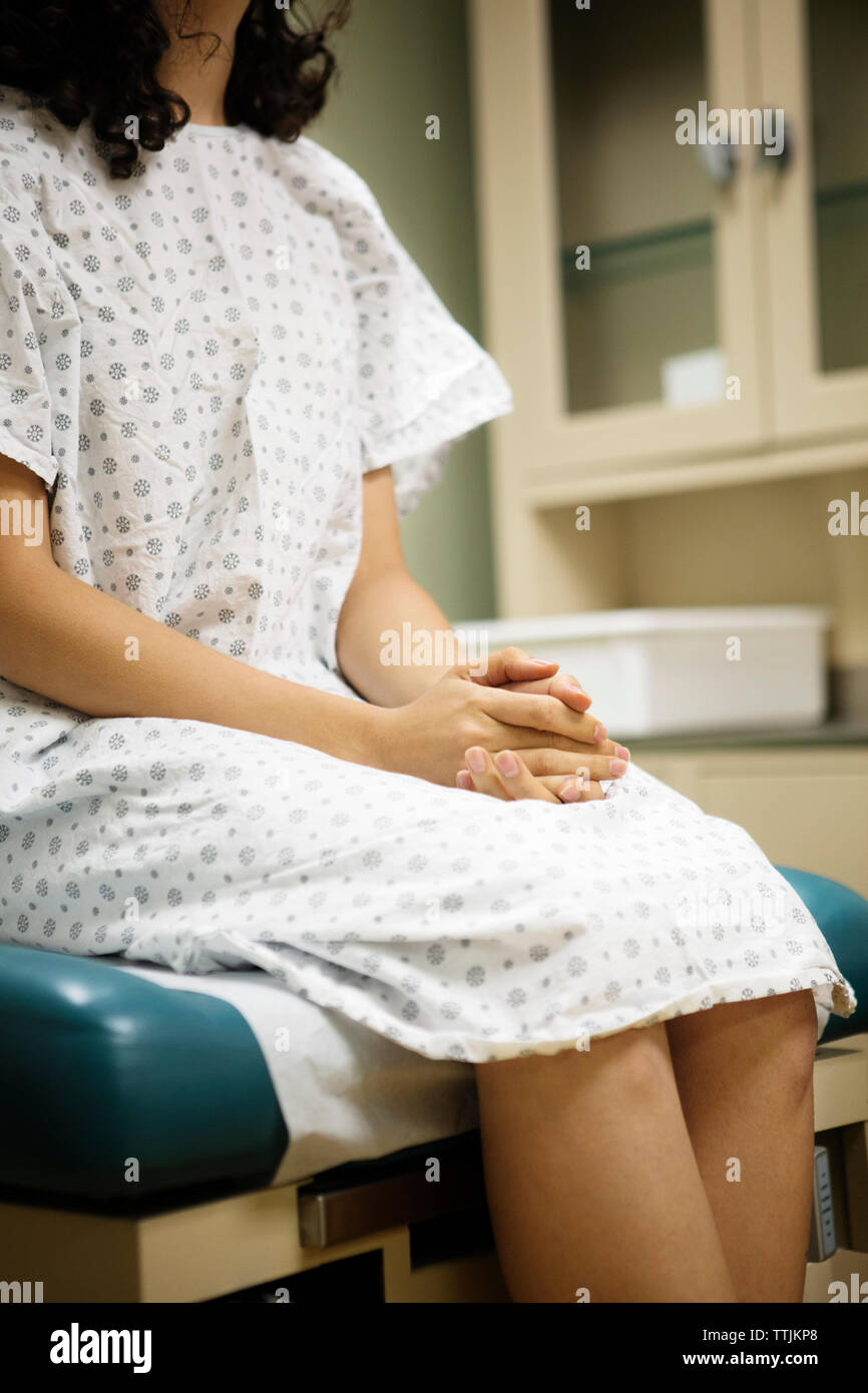 Midsection of woman with hands clasped sitting on bed in hospital Stock Photo