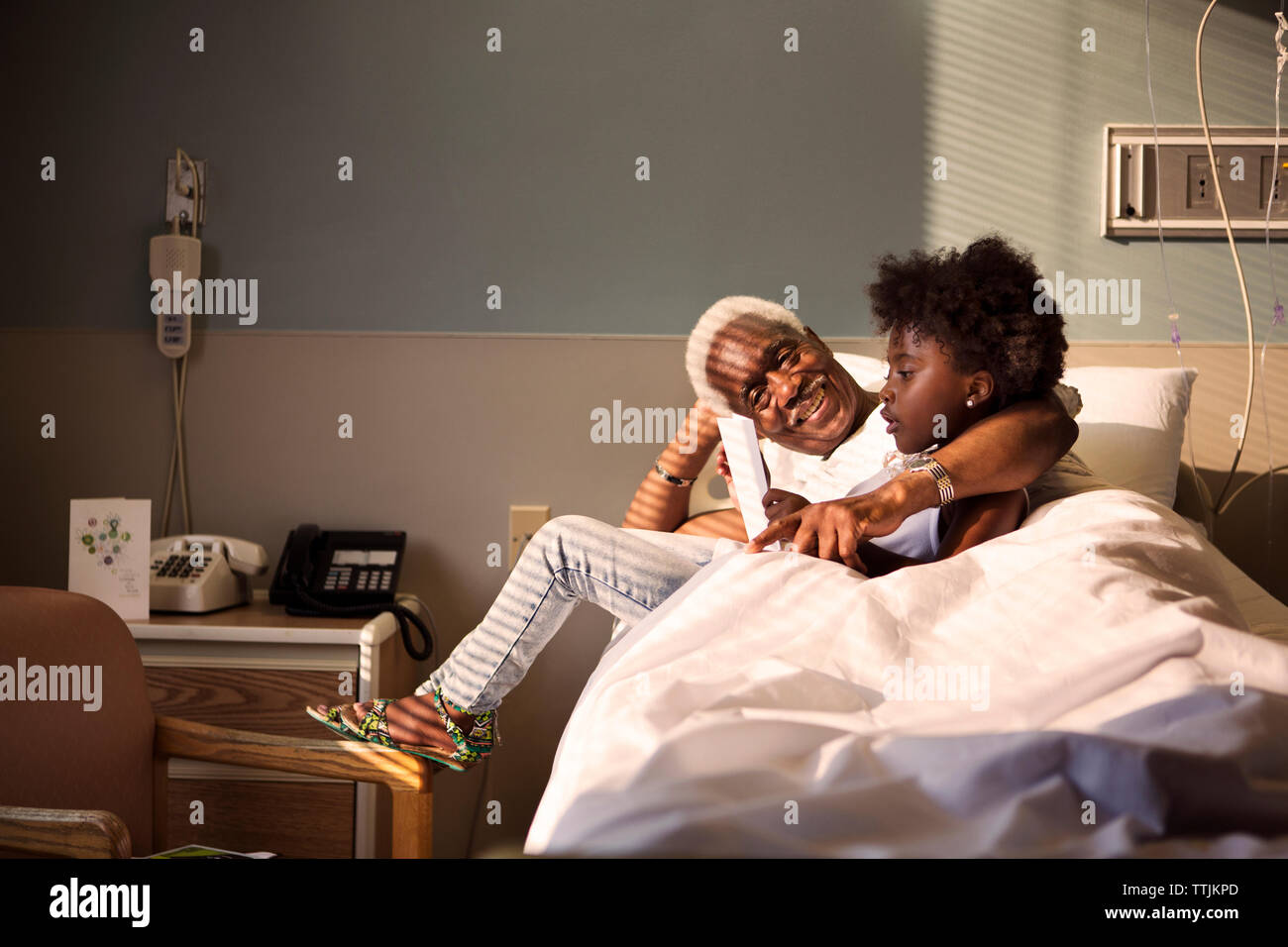 Girl with grandfather on bed in hospital Stock Photo