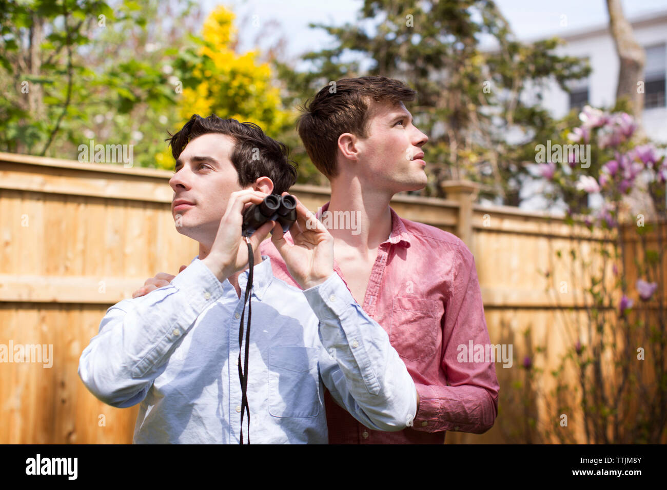 Gay men with binocular looking away while standing in backyard Stock Photo