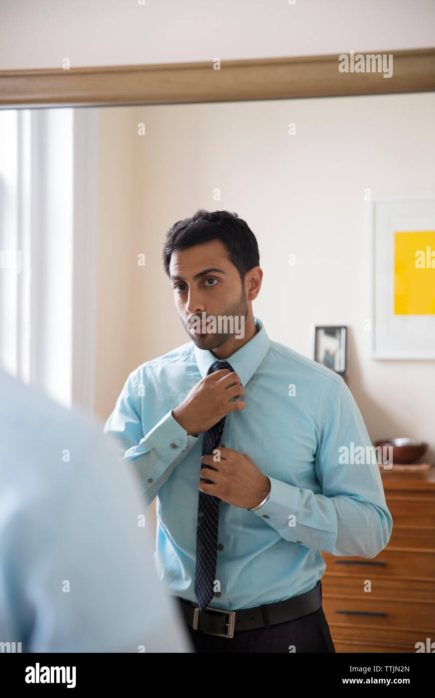 Man adjusting necktie while standing in front of mirror at home Stock Photo