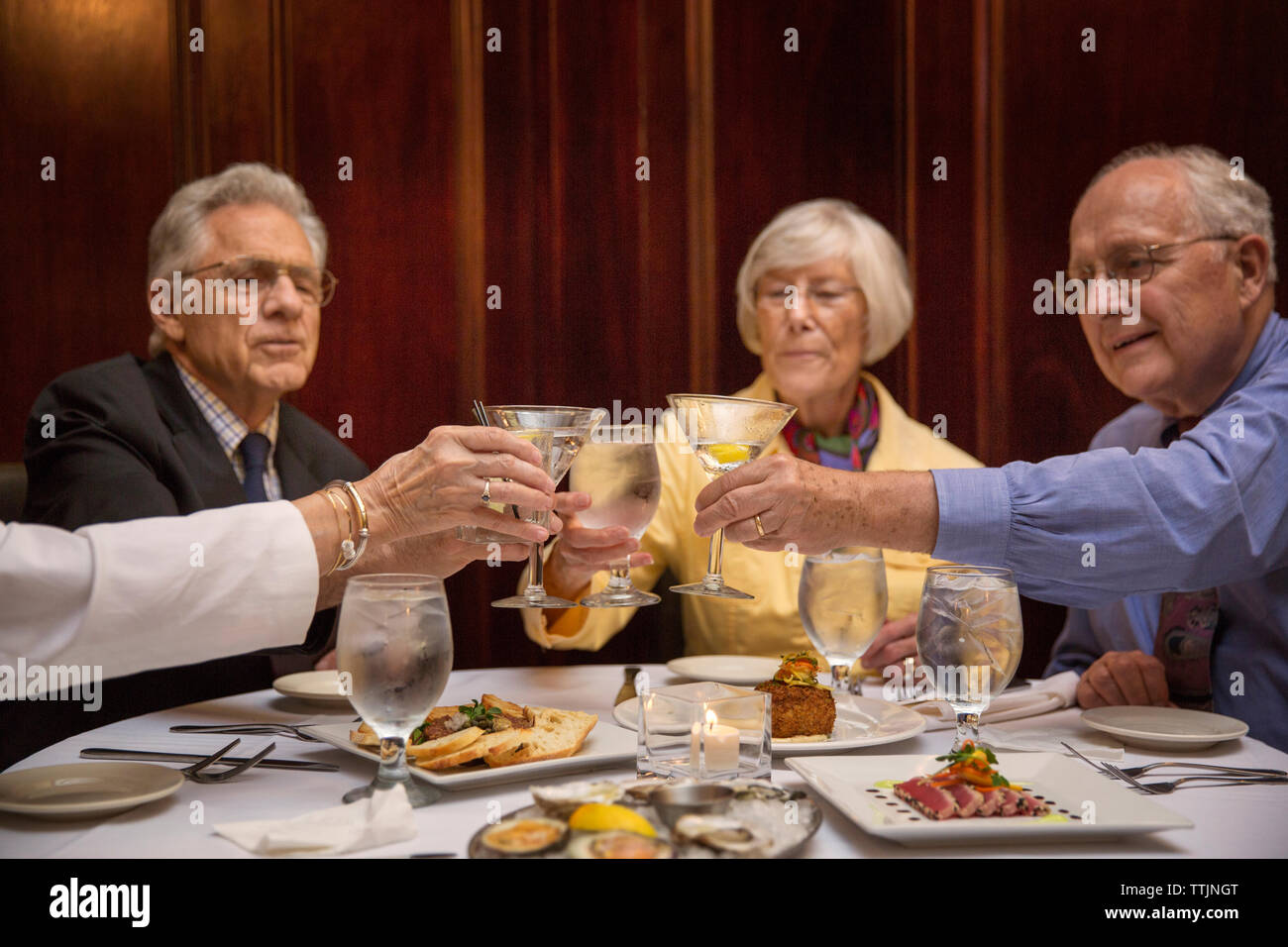 Senior friends toasting martini glasses while sitting in restaurant Stock Photo