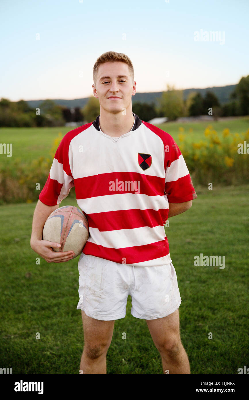 Portrait of confident player holding rugby ball on field against clear sky Stock Photo