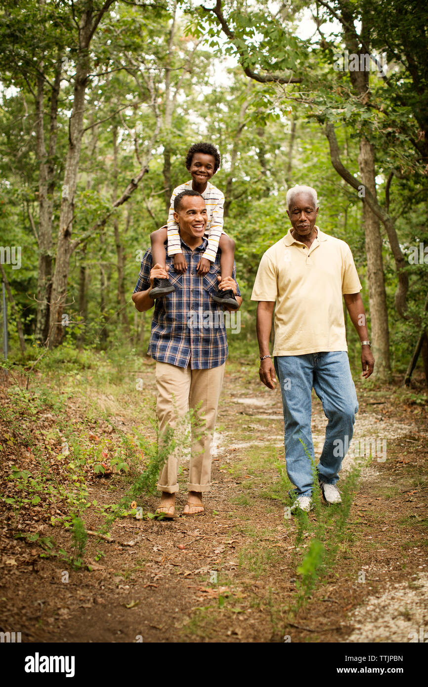 Man carrying son on shoulders while walking with father in forest Stock Photo