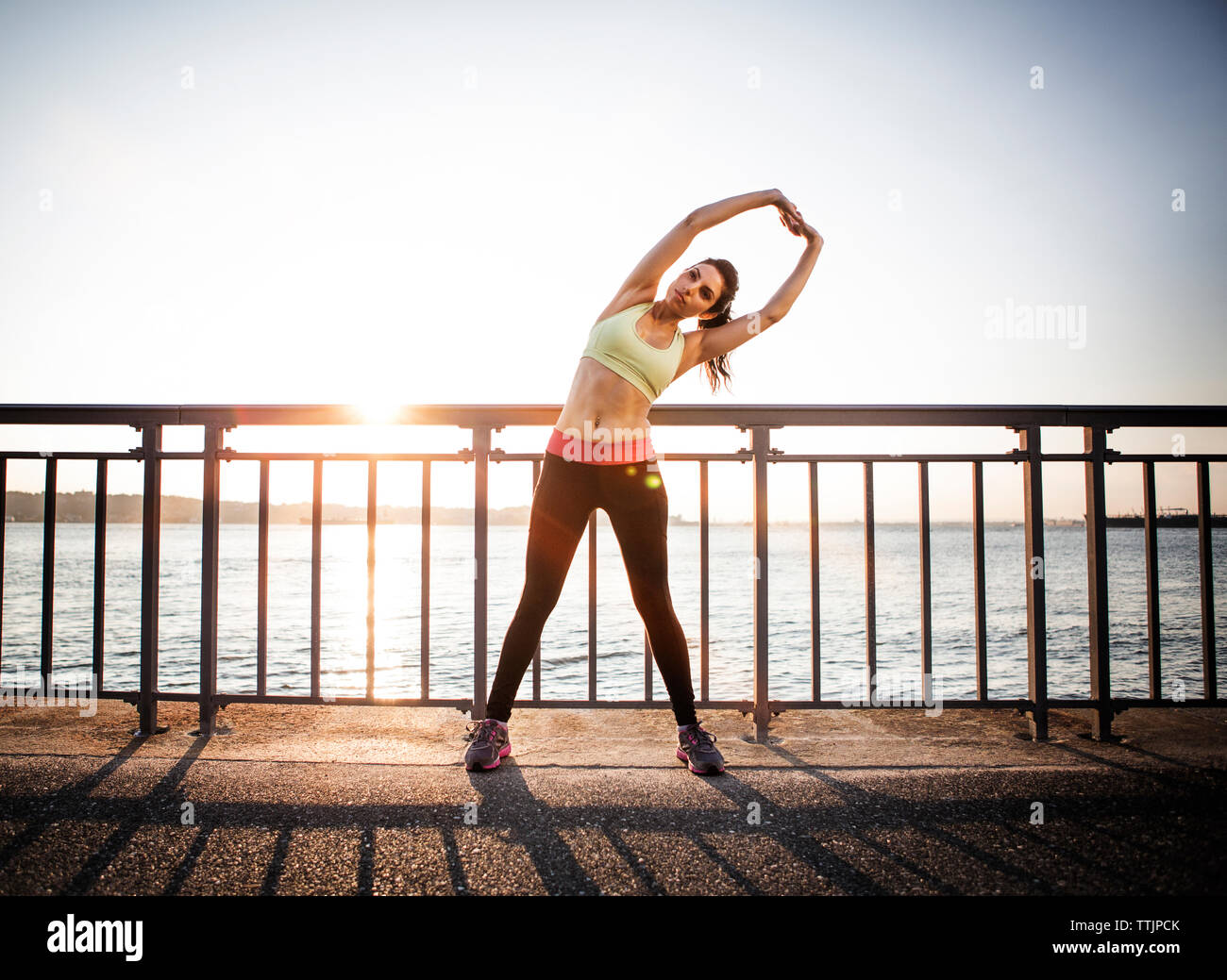 Athlete stretching with arms raised at railing by river against sky Stock Photo