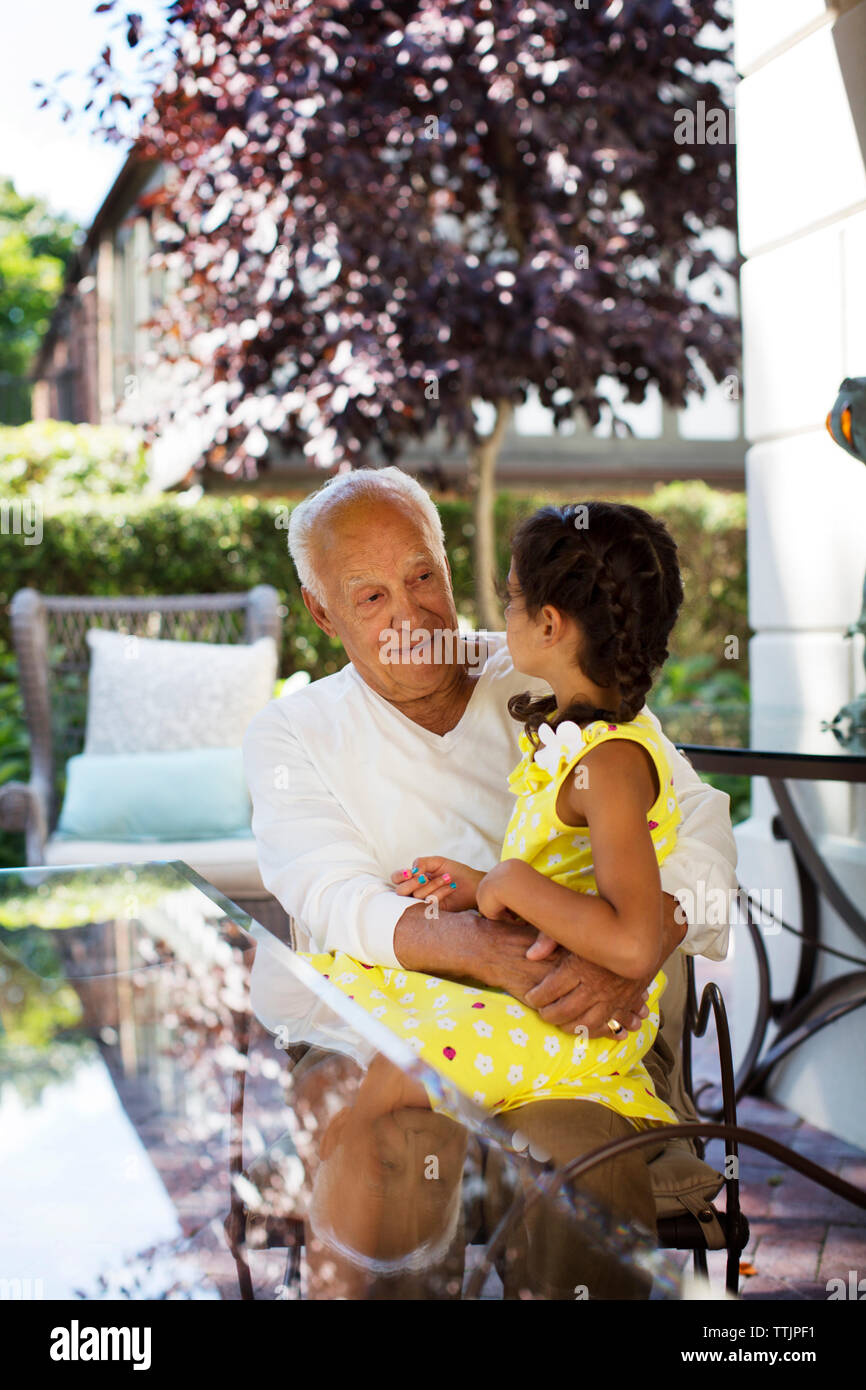 Girl sitting on grandfather's lap by table at home Stock Photo