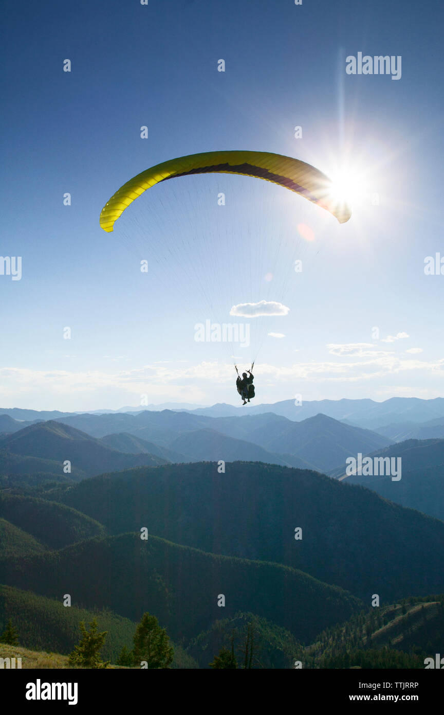 Silhouette person paragliding over mountains against bright sky Stock Photo