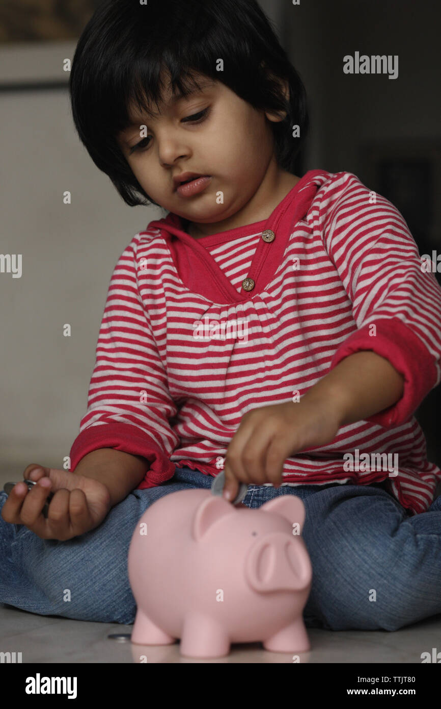 Girl putting a coin into a piggy bank Stock Photo - Alamy