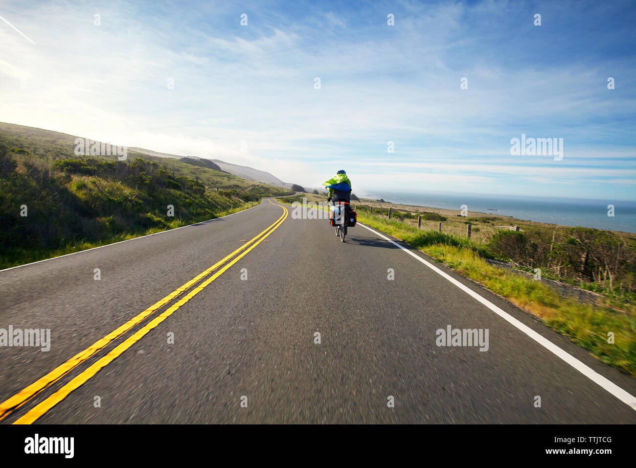 Rear view of cyclist on country road against sky Stock Photo