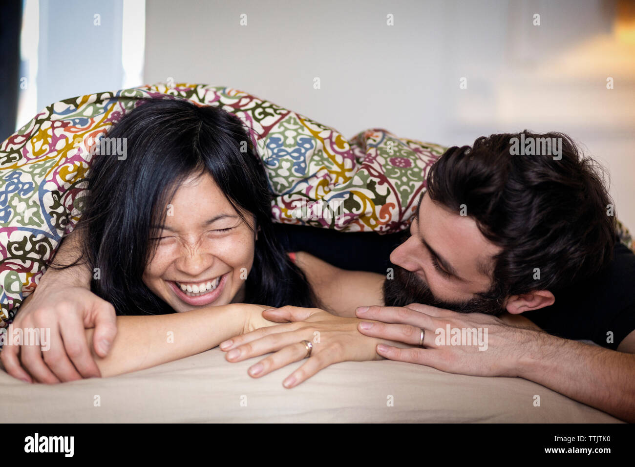 Happy couple talking while lying on bed at home Stock Photo