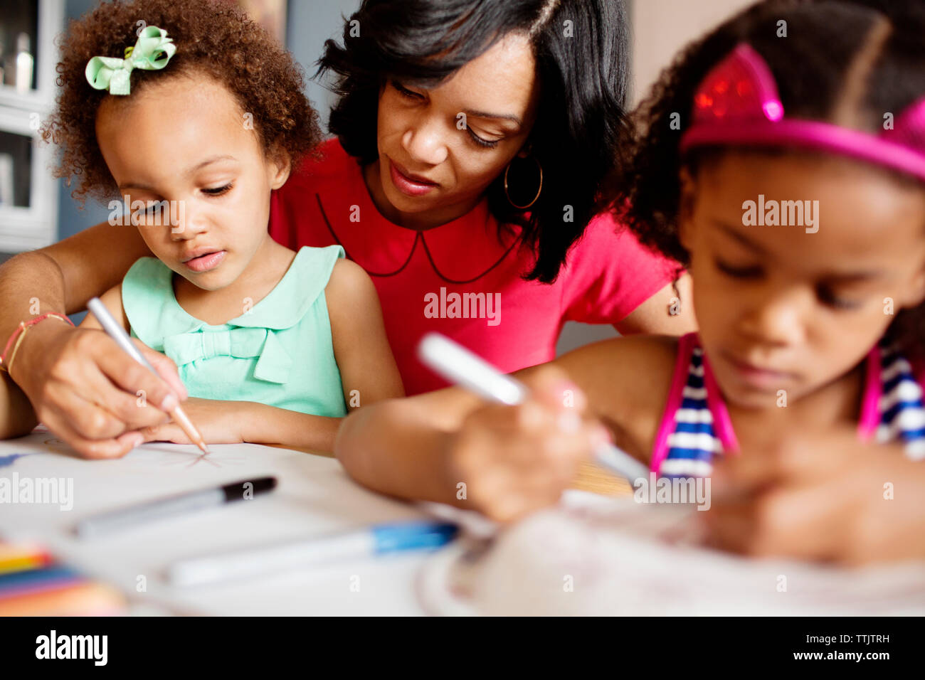 Mother assisting daughters in drawing at table Stock Photo