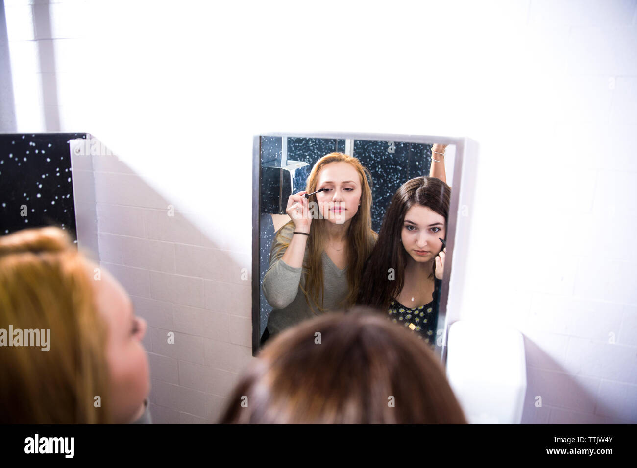 Friends doing make-up in restroom at high school seen through mirror Stock Photo