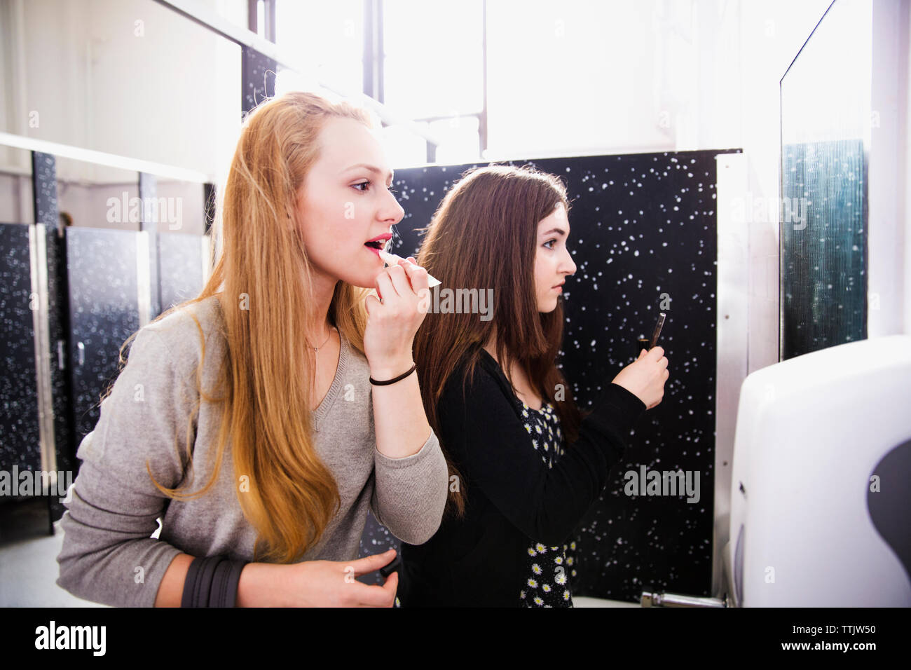 Friends doing make-up in restroom at high school Stock Photo