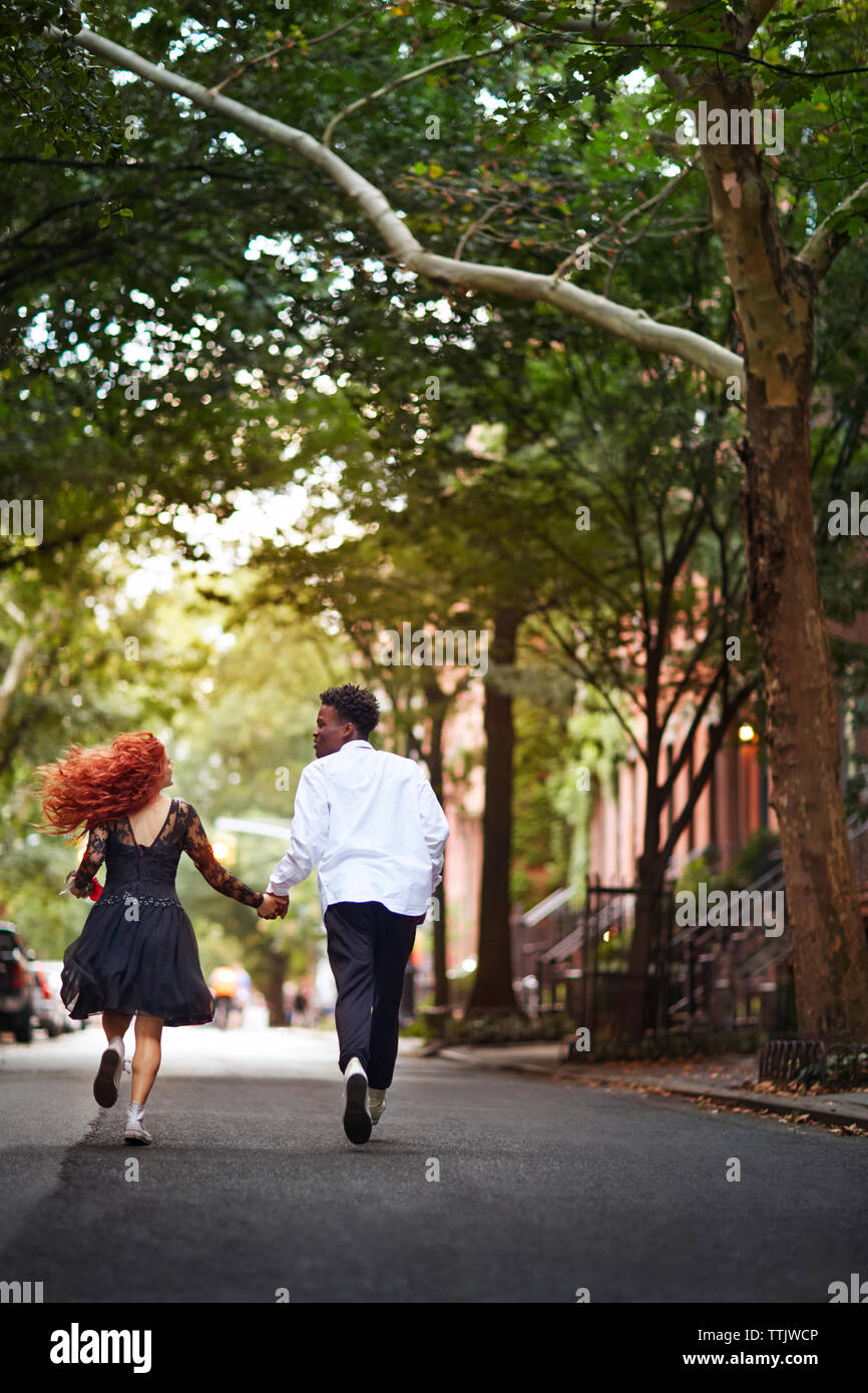 Rear view of couple holding hands and running on street Stock Photo - Alamy