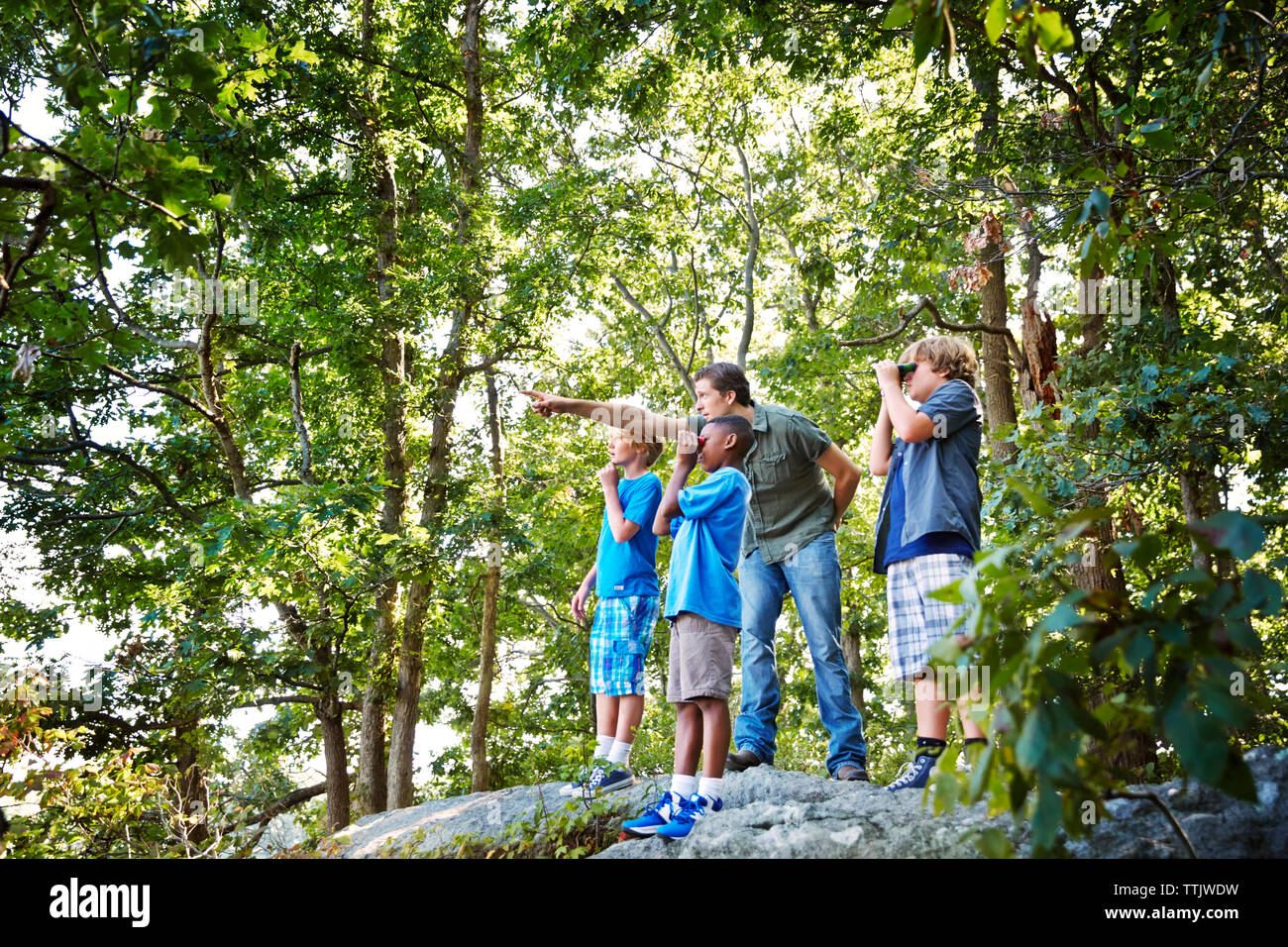 Teacher explaining students while standing on rocks in forest during ...