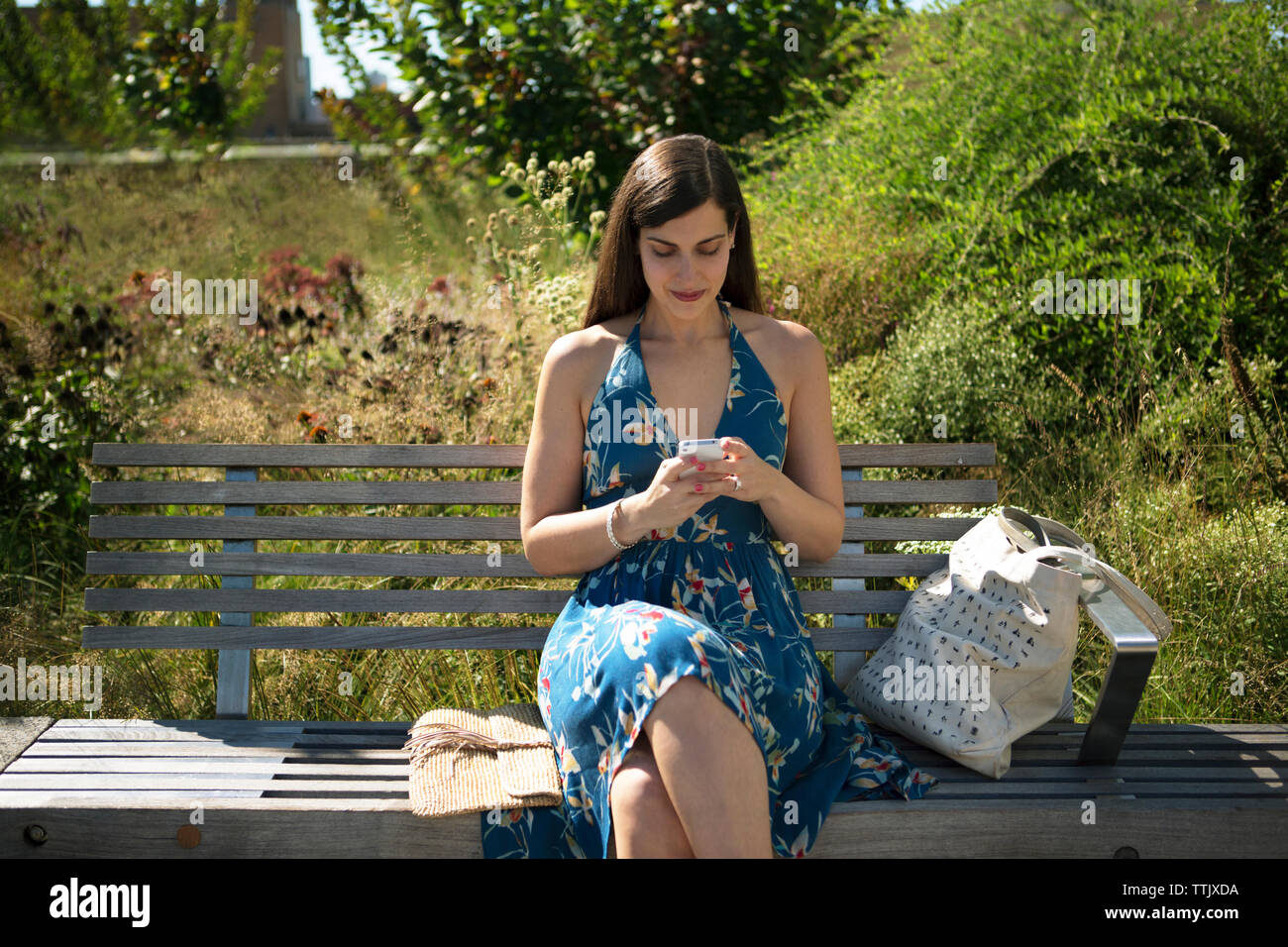 Woman using smart phone while sitting on bench at park Stock Photo