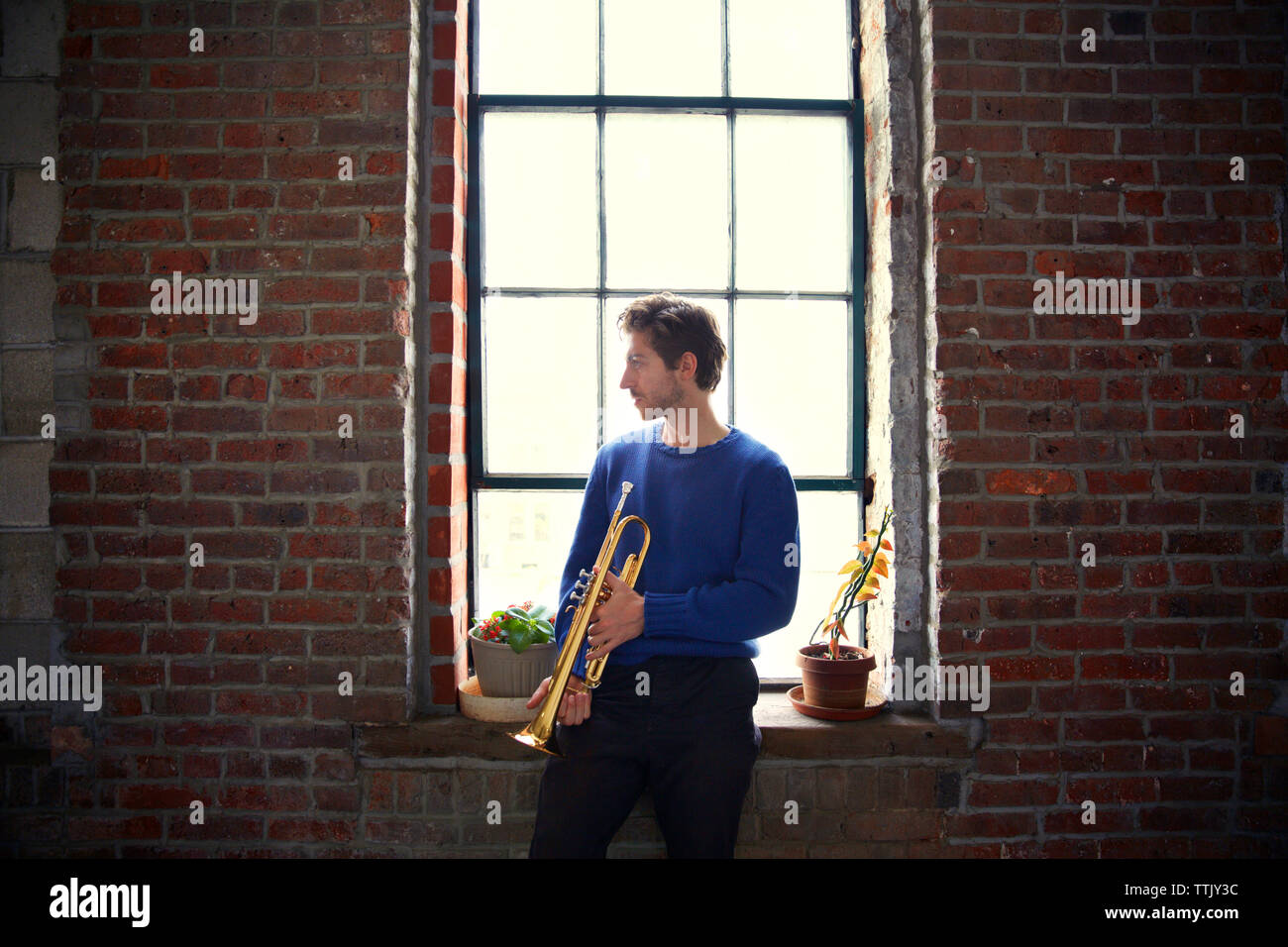 Man with trumpet looking away while standing by window Stock Photo