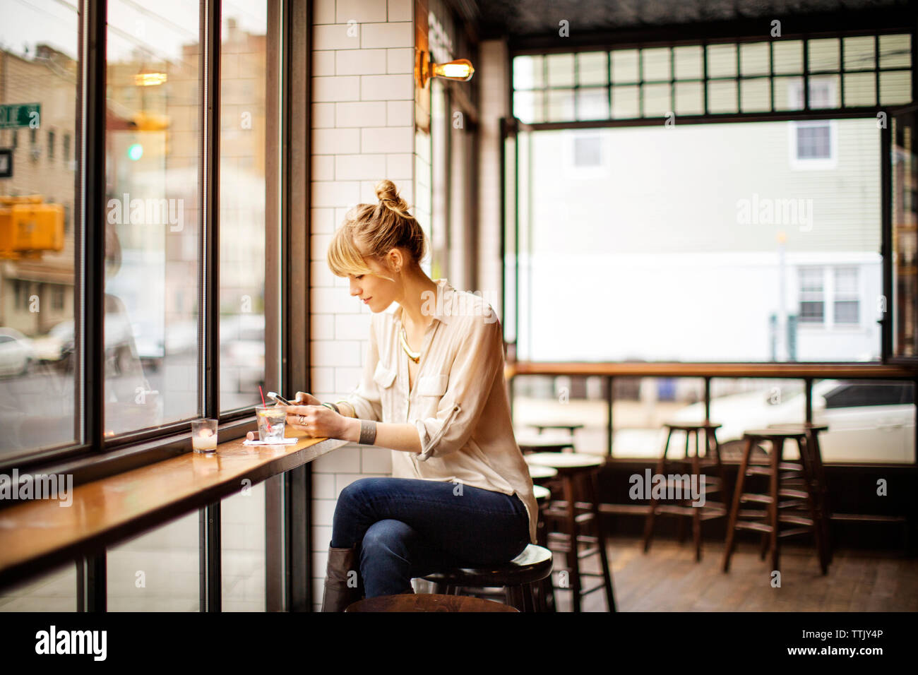 Woman using smart phone while sitting on stool in bar Stock Photo