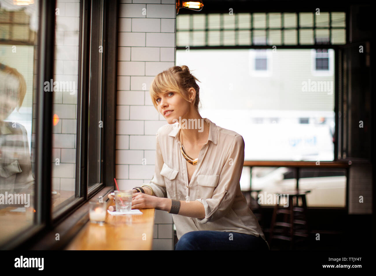 Woman looking away while sitting on stool in bar Stock Photo