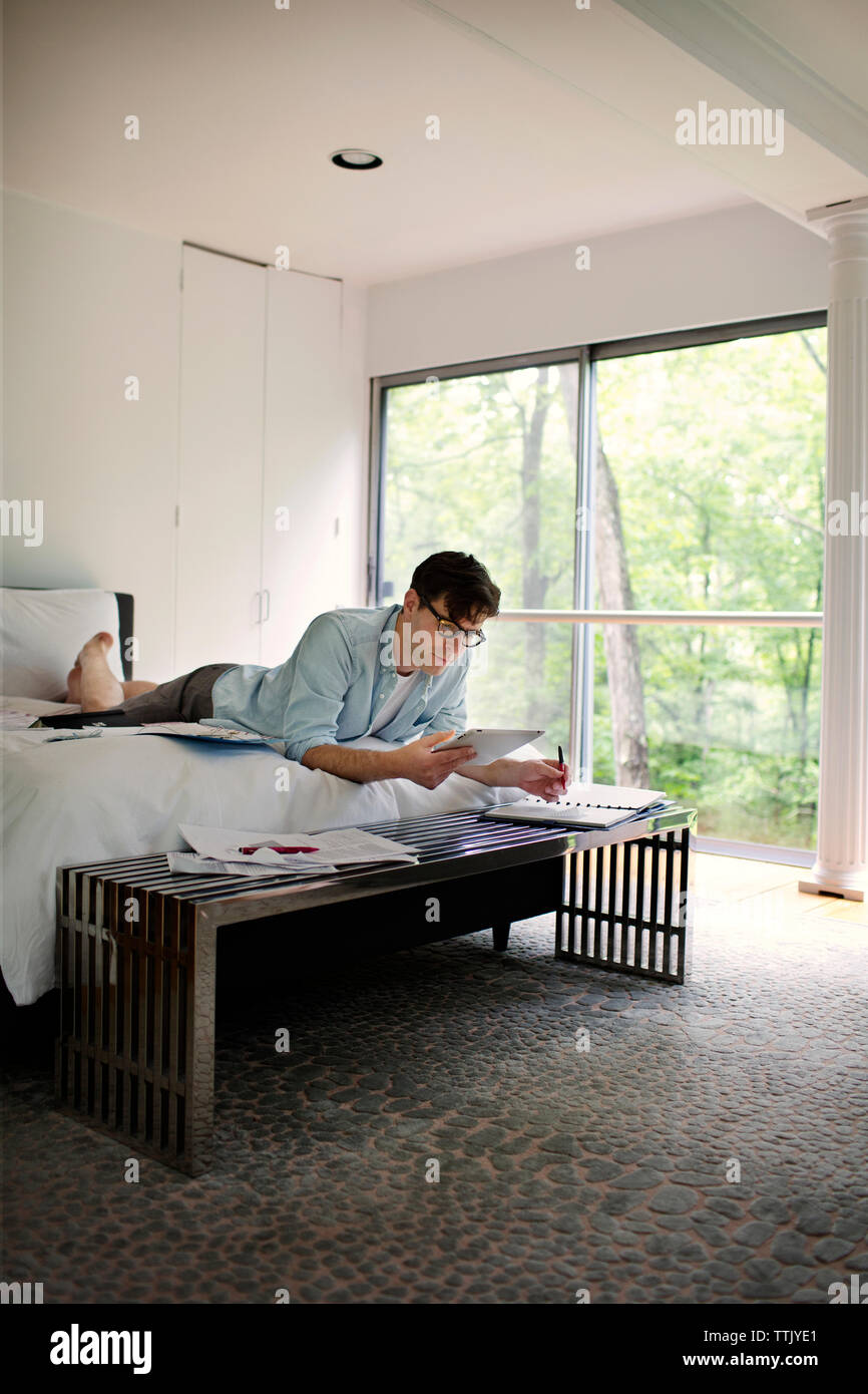 Man using tablet computer while working on bed at home Stock Photo