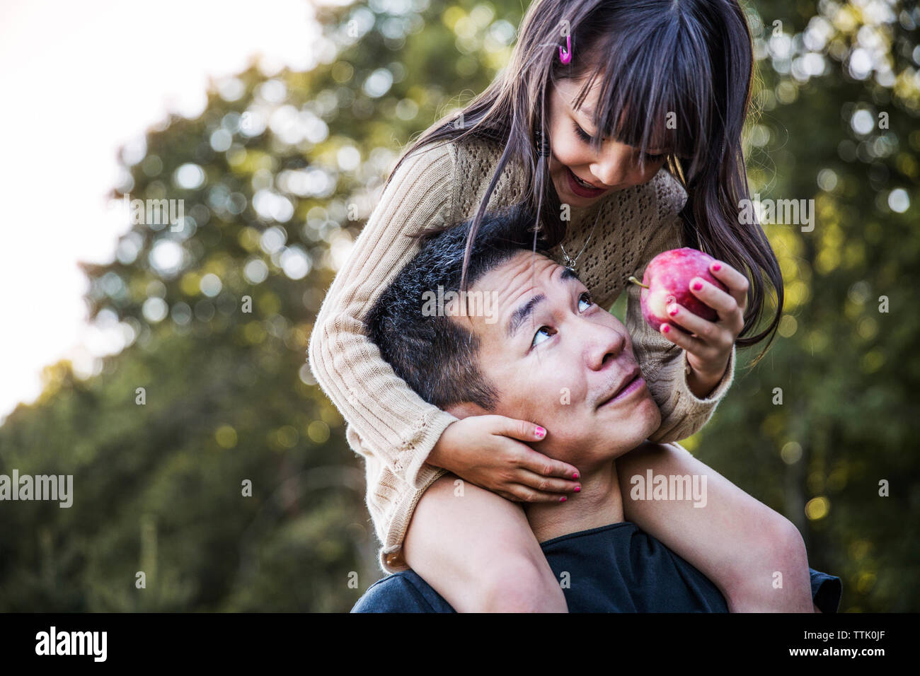 Girl sitting on father's shoulder in orchard Stock Photo