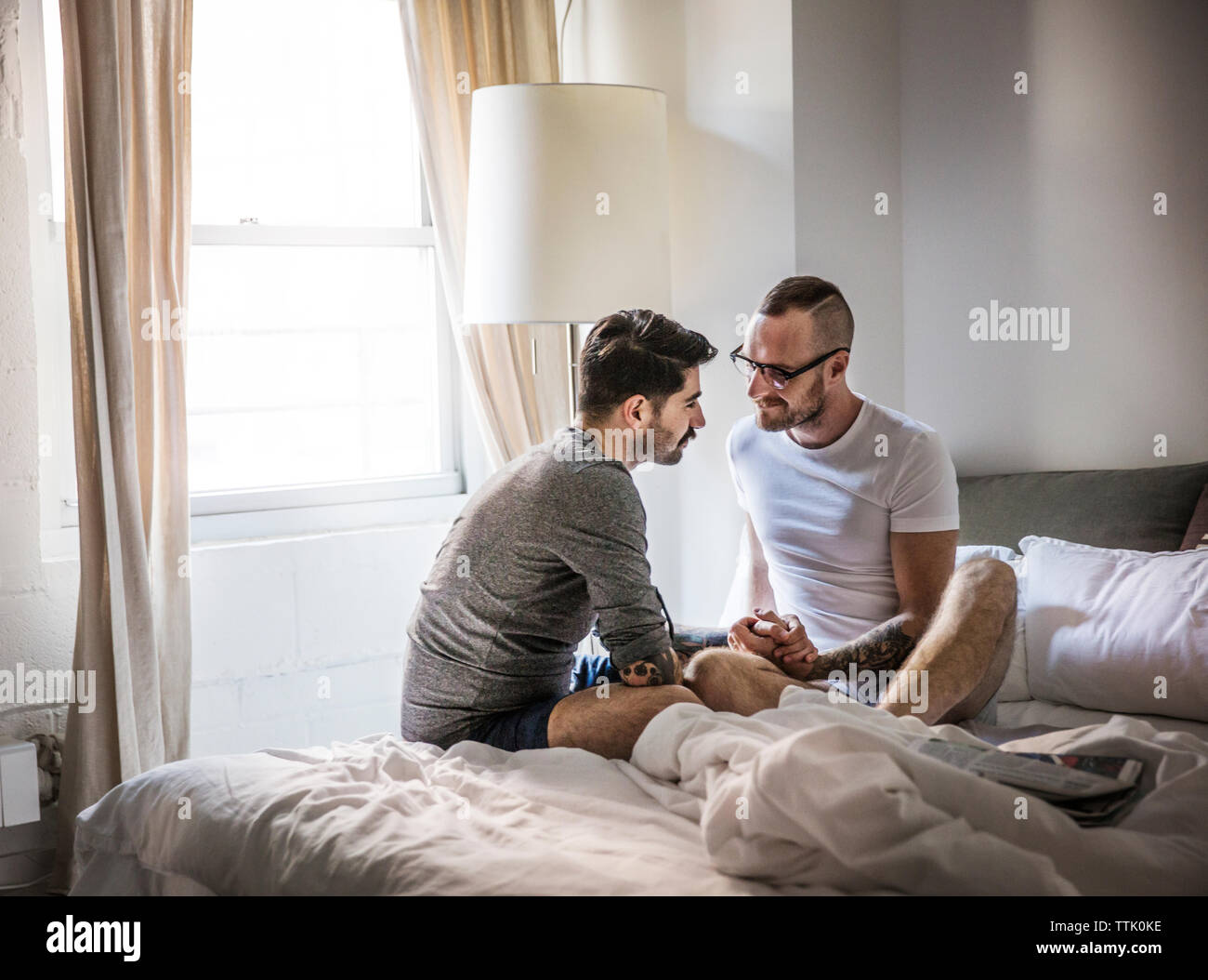 Gay men holding hands while sitting on bed at home Stock Photo