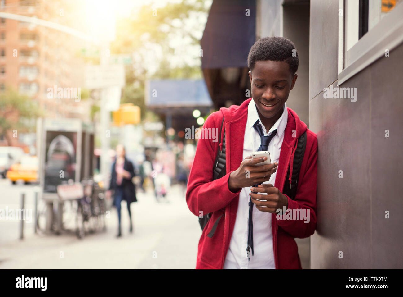 Smiling student using phone while leaning on wall in city Stock Photo