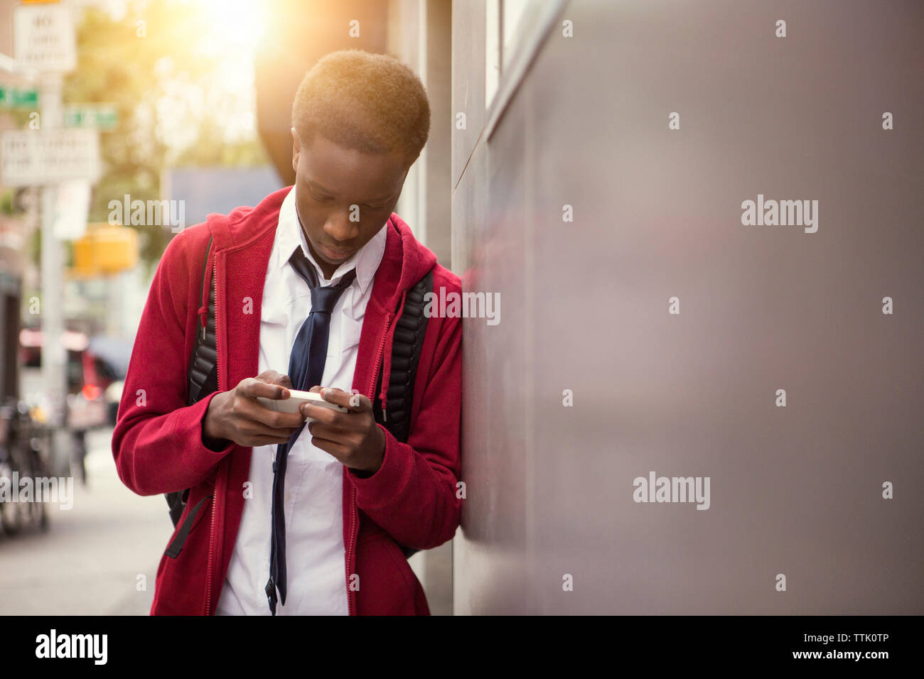student using phone while leaning on wall in city Stock Photo