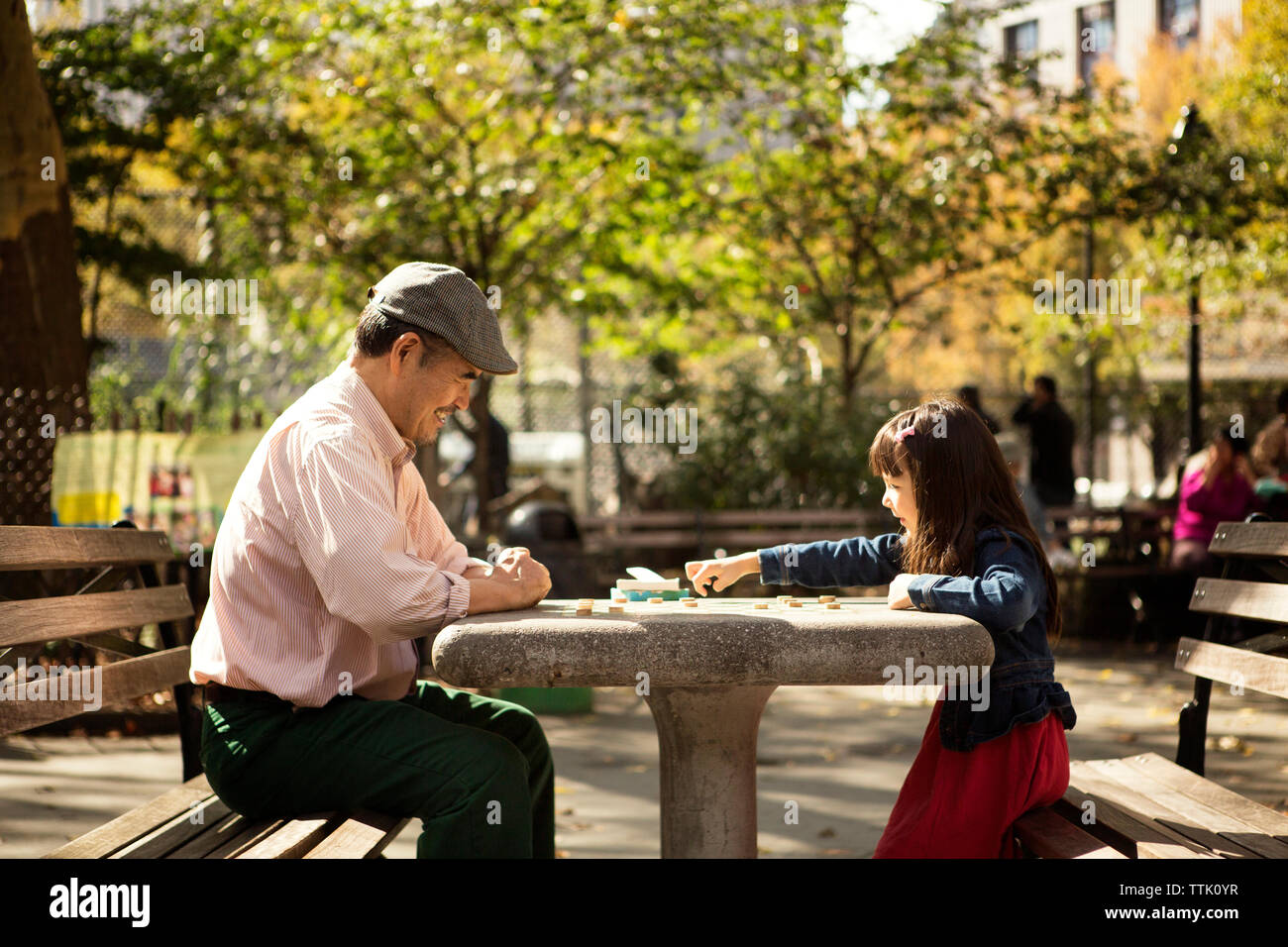 Grandfather and granddaughter playing board game while sitting at table in park Stock Photo