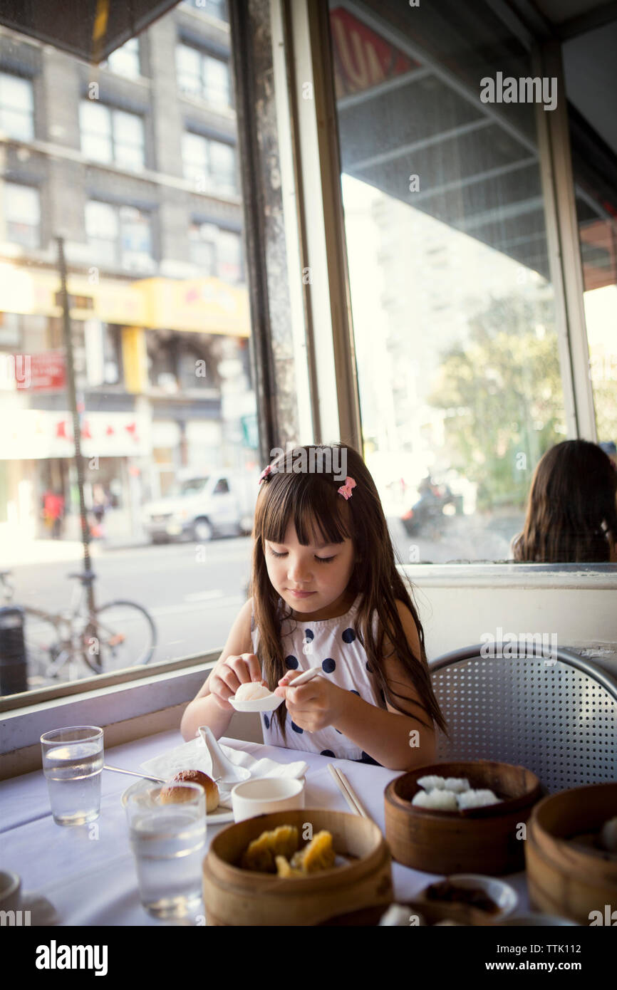 Girl looking at dumpling in spoon while sitting in restaurant Stock ...