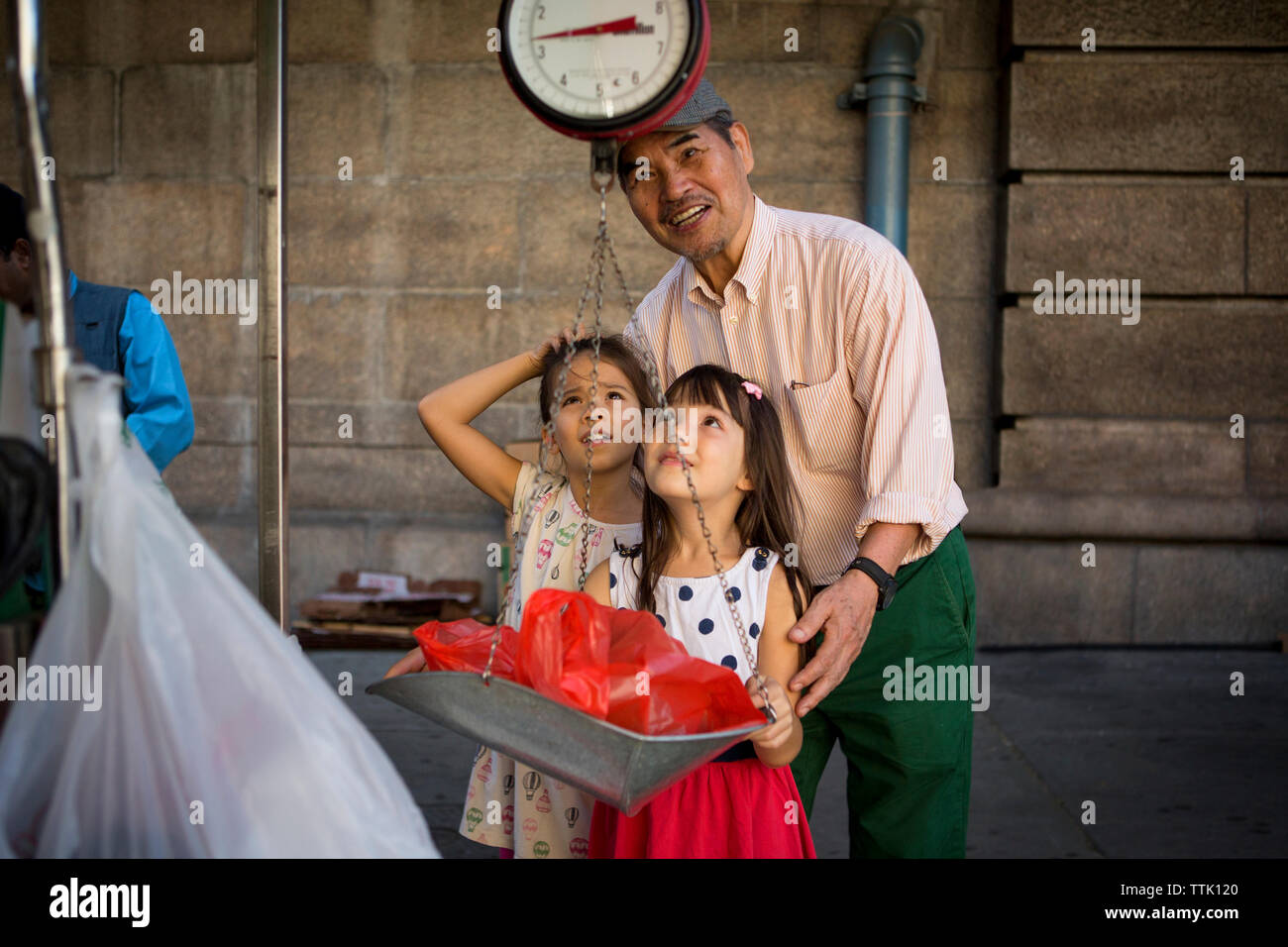 Granddaughters with grandfather weighting bag on scale at stall in market Stock Photo