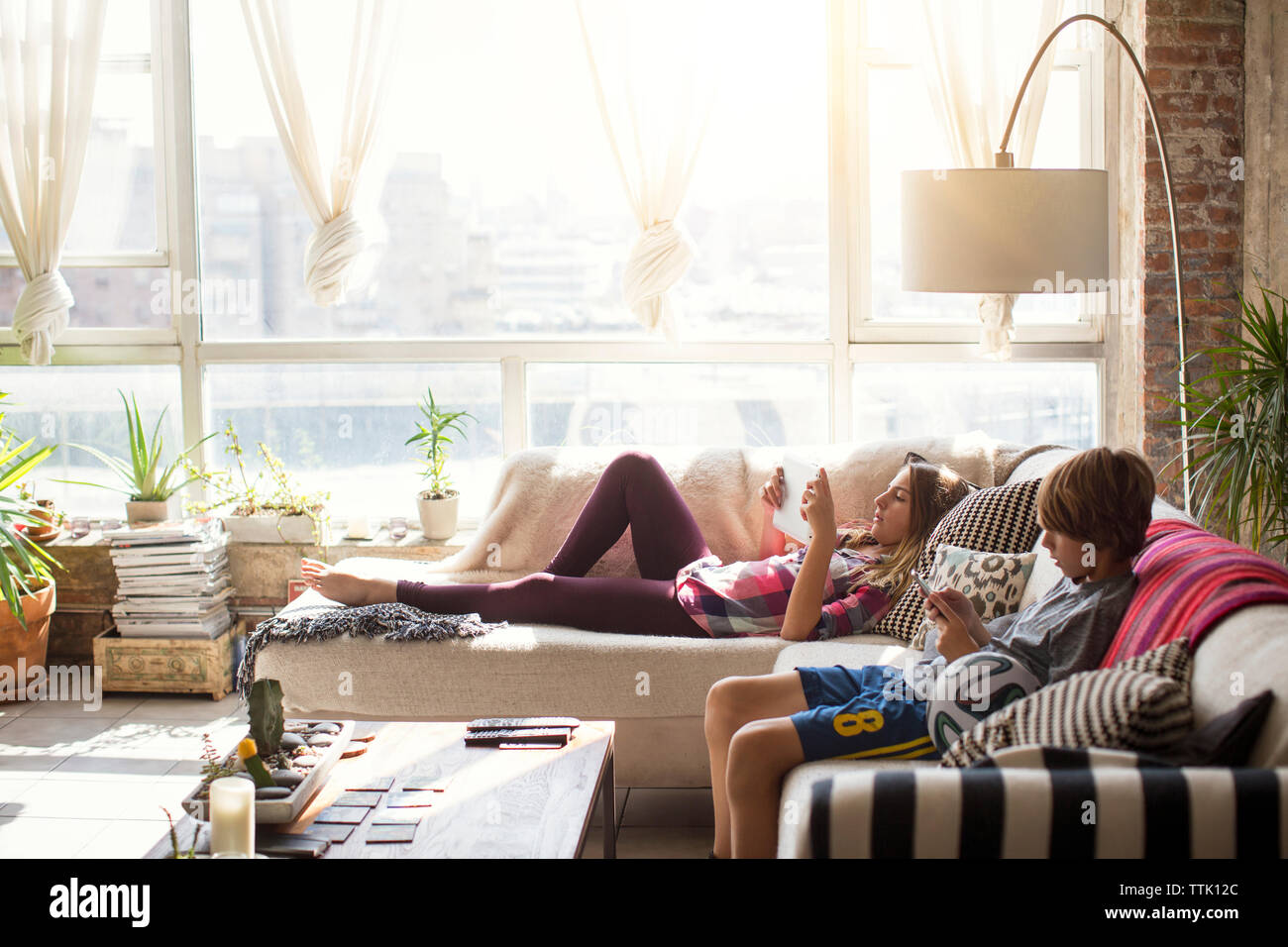 Siblings using technologies while relaxing in living room Stock Photo