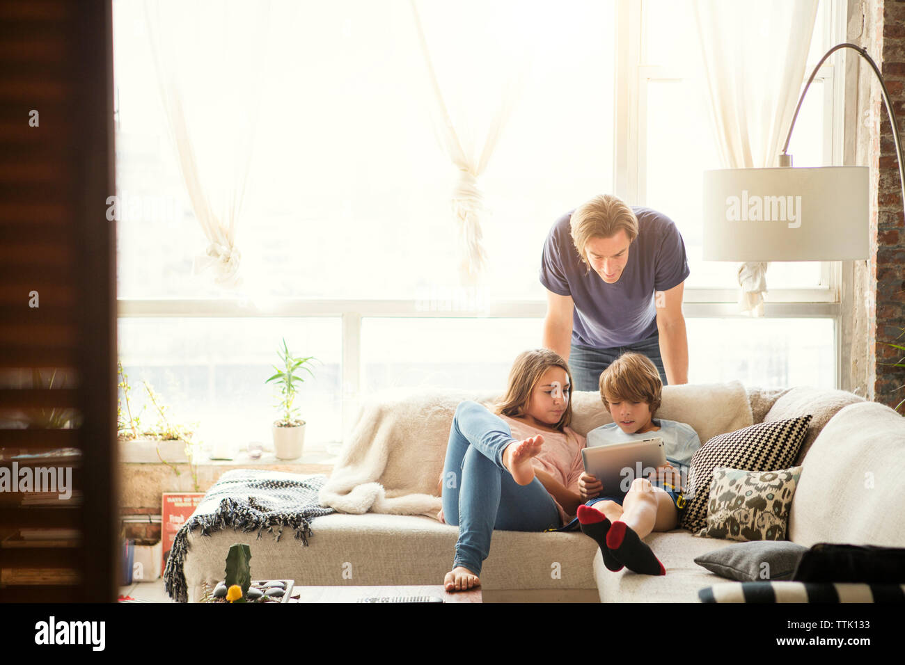 Father looking at children using tablet computer at home Stock Photo
