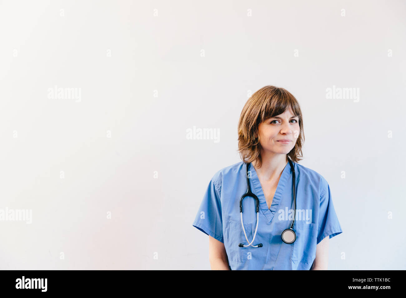 Portrait of female doctor with stethoscope standing against white ...