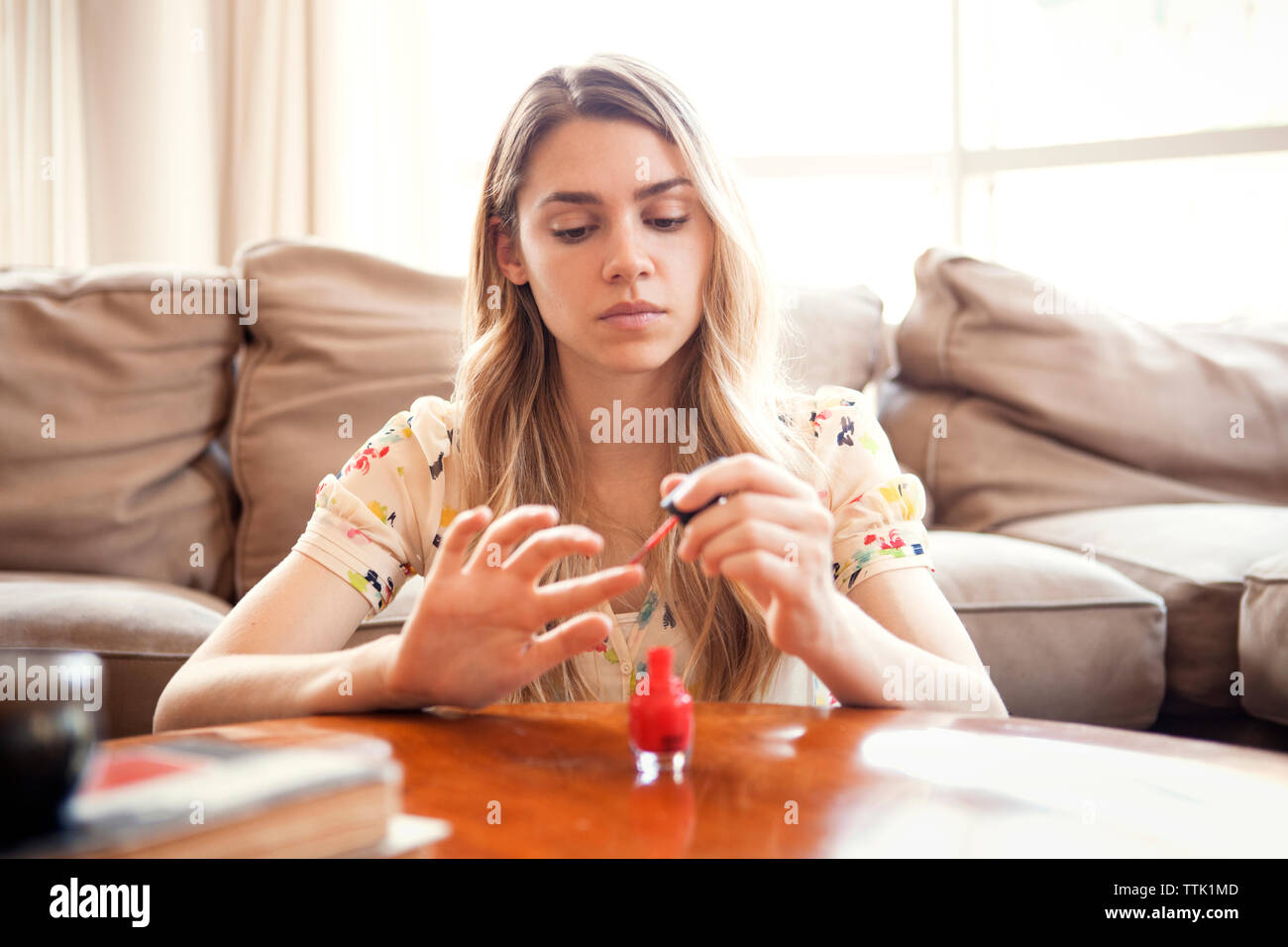 Woman applying nail polish while sitting against sofa at home Stock Photo