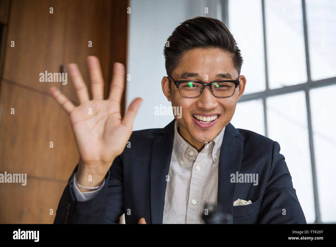 Happy businessman waving while sitting at office Stock Photo