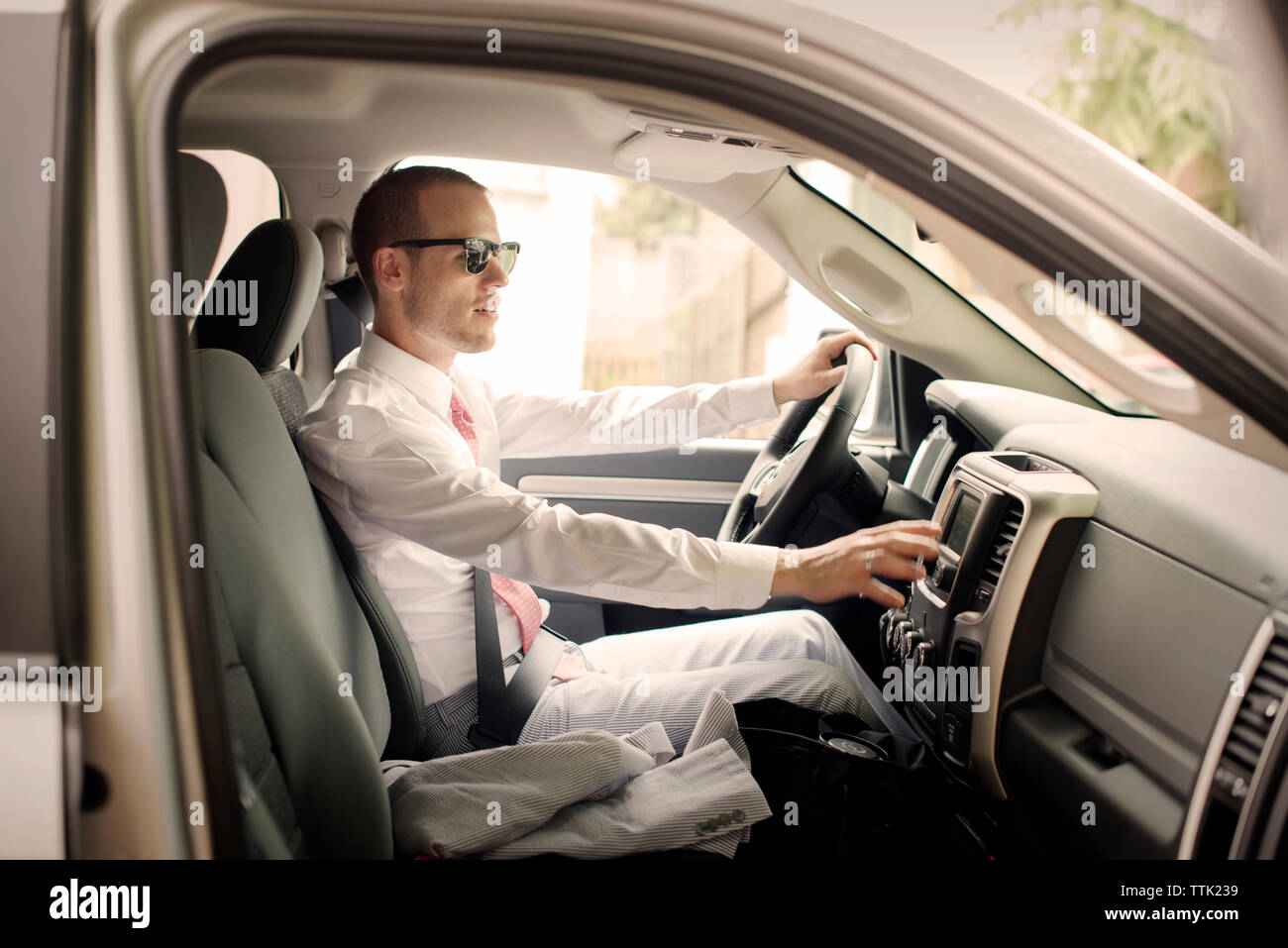 Side view of gay man wearing suit riding car on sunny day Stock Photo