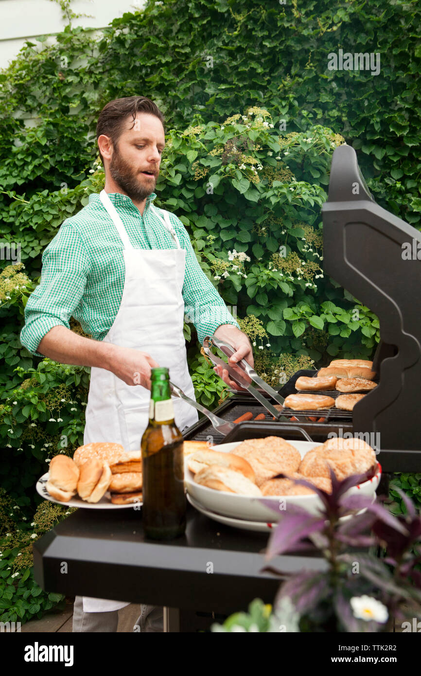 Man preparing food on barbecue grill while standing in yard Stock Photo