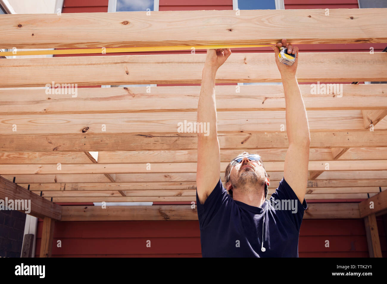Carpenter measuring plank while standing in yard Stock Photo