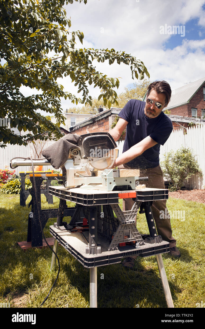 Man cutting wood at table saw while standing in yard Stock Photo