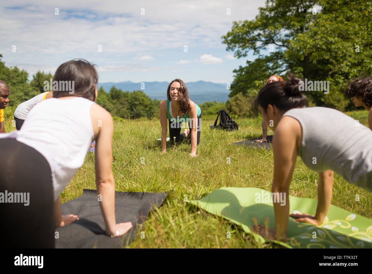 Friends practicing downward facing dog position while exercising on field Stock Photo