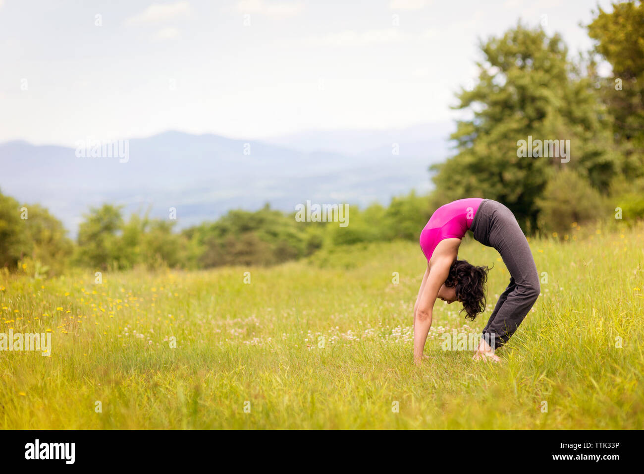 Side view of woman bending over backwards on grassy field Stock Photo